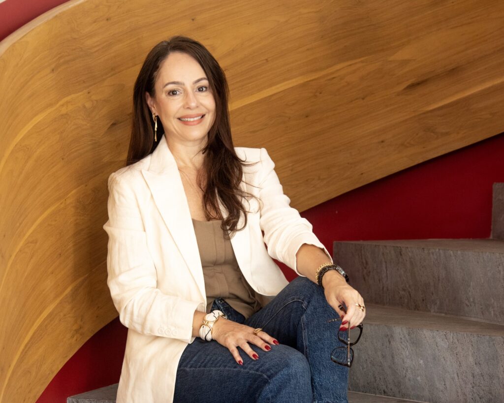 Olga Portela, arquiteta, sorrindo enquanto está sentada, destacando seu trabalho com arquitetura ao pensar na iluminação natural da sua casa.